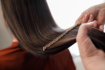 Gros plan des mains de maître de coiffure peignant les cheveux longs avec une brosse à cheveux spéciale
