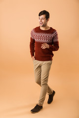 Full length image of handsome man 20s with bristle wearing knitted sweater smiling while walking,...