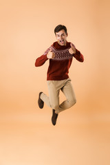Full length image of cheerful man 20s with bristle wearing knitted sweater jumping and rejoicing,...