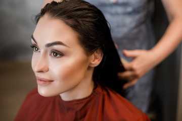 Top view of young tender girl sitting in terracotta cape and waiting for wonderful styling in beauty salon