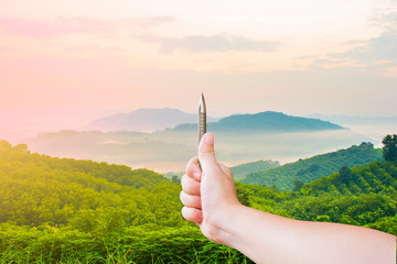 A hands are holding pen perpendicular to the nature to measure with the mountain