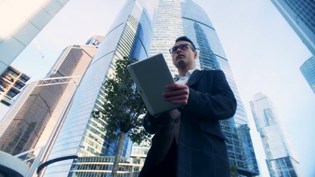 Business street with a male specialist walking along it and holding a tablet. Red epic dragon 6K shot.
