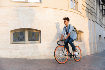 Happy young african guy walking with bicycle outdoors on the street.