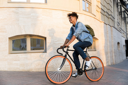 Happy young african guy walking with bicycle outdoors on the street.