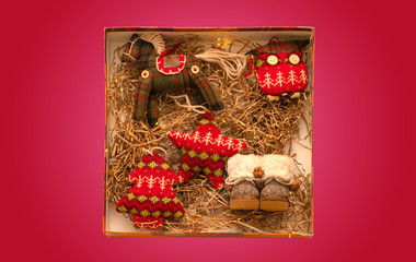 Vintage rag knitted Christmas toys in a box with thatched bedding and lights. Retro style. Isolate on red background.