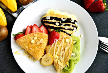 Variety mixed fruits crepes and many kind syrup with almond slices on black dish with fresh bananas on black