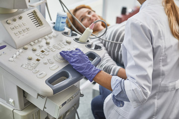 Gynecologist in white lab coat and sterile gloves using ultrasound scanner during medical...