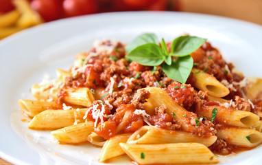 Penne  bolognese with basil leaf on white plate.