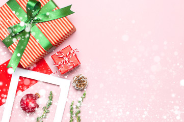 Snowy Christmas composition. White photo frame, red envelope, fir branches, cones ball twine gift wooden toys on pink background Flat lay top view. Christmas winter decoration New Year holiday objects