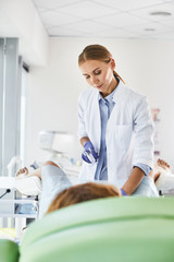 Vertical portrait of gynecologist in white lab coat and sterile gloves using vaginal speculum during pelvic exam