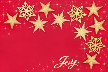 Christmas abstract background with gold joy sign and sparkling star bauble decorations on red with copy space. Traditional festive card for the Christmas holiday season.