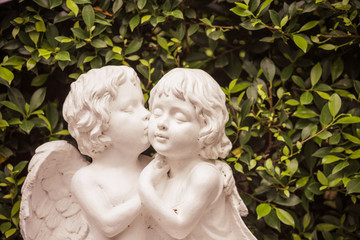 Vintage style cute cupid kiss angel statue in green garden, valentine romantic day