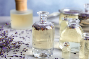Bottles with natural herbal oil and lavender flowers on color table, closeup