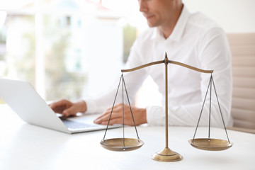 Scales of justice and blurred notary with laptop on background