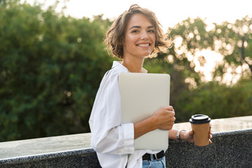 Beautiful woman walking outdoors holding laptop computer holding coffee.