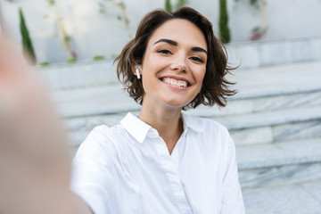 Cheerful young woman in earphones standing at the street