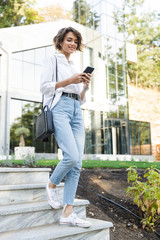 Cheerful young woman in earphones walking downstairs