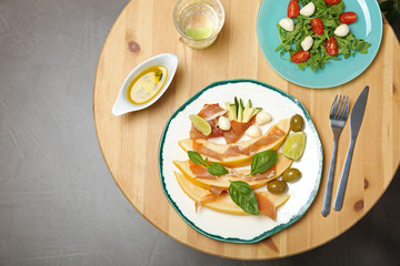 Flat lay composition with melon and prosciutto appetizer served on wooden table