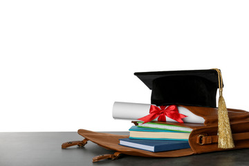 Briefcase with books, diploma and graduation hat on table against white background