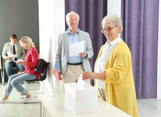 Fototapeta premium Elderly woman putting ballot paper into box at polling station