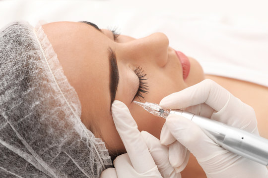 Young woman undergoing procedure of permanent eye makeup in tattoo salon, closeup