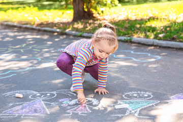 Little child drawing with colorful chalk on asphalt