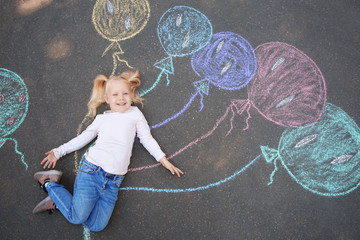 Little child lying near chalk drawing of balloons on asphalt, top view
