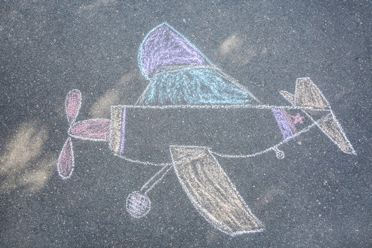 Child's chalk drawing of airplane on asphalt, top view