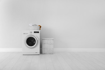 Washing machine with laundry and basket near wall. Space for text - obrazy, fototapety, plakaty