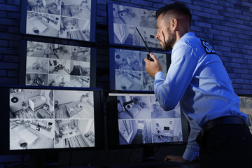Male security guard with portable transmitter monitoring modern CCTV cameras indoors