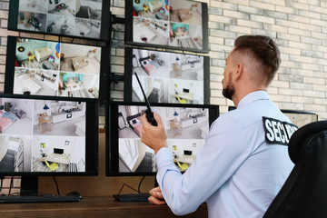 Male security guard with portable transmitter monitoring modern CCTV cameras indoors