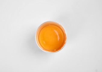 Cracked raw chicken egg with yolk on white background, top view