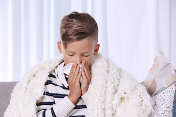 Ill boy suffering from cough on sofa at home