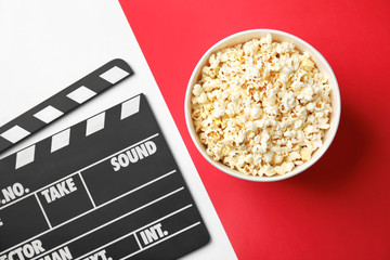 Tasty popcorn in paper cup and clapperboard on color background, top view. Cinema snack