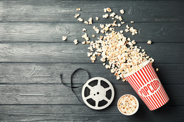 Tasty popcorn and film reel on wooden background, top view with space for text. Cinema snack