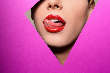 Naklejka premium View of beautiful young woman with red lips through cutout in color paper, closeup