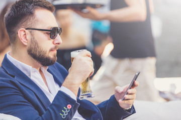 Fashionable man drinking beer and holding smartphone in pub.