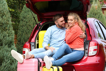 Happy young couple sitting in car trunk and suitcases outdoors