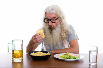 Studio shot of senior bearded man holding and looking at potato 