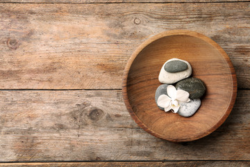 Plate with spa stones and space for text on wooden background, top view