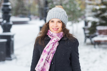 Winter and people concept - portrait of young woman in hat and scarf smiling outdoors