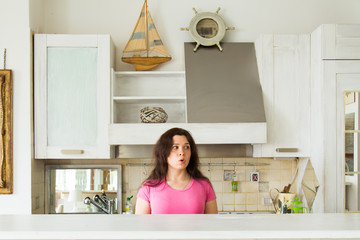 Housewives, emotions and people concept - Surprised young woman in the kitchen at home