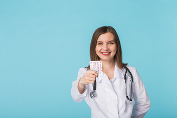 Attractive female doctor showing pink pills. Beautiful young physician holding medicaments over blue background with copy space