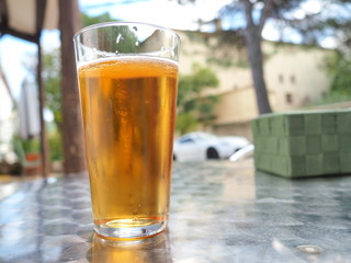 Cerveza fría servida en vaso de cristal sobre mesa metálica en terraza.
