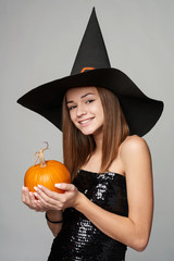 Serious Halloween witch holding orange pumpkins looking at camera with a look of suspect, isolated...
