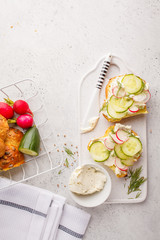 Breakfast cream cheese, cucumber and radish sandwiches on a white board, top view.