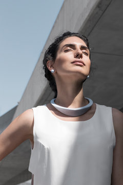 Beautiful woman with minimalist jewelry and outfit under the sun in concrete architecture site