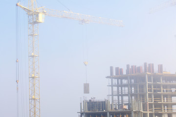 Fototapeta na wymiar Tower cranes on the construction of a building with a frame of reinforced concrete. Works in the morning mist.
