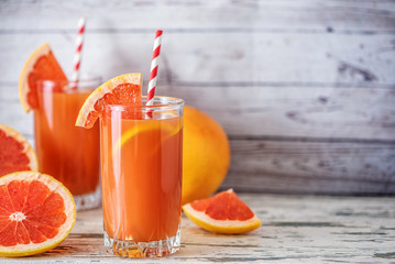 Fresh grapefruits and two glasses of grapefruit juice on light wooden table. With copy space