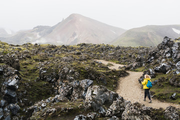 Woman in yellow raincoat walking through the lava field in Landmannalaugar national park, Iceland